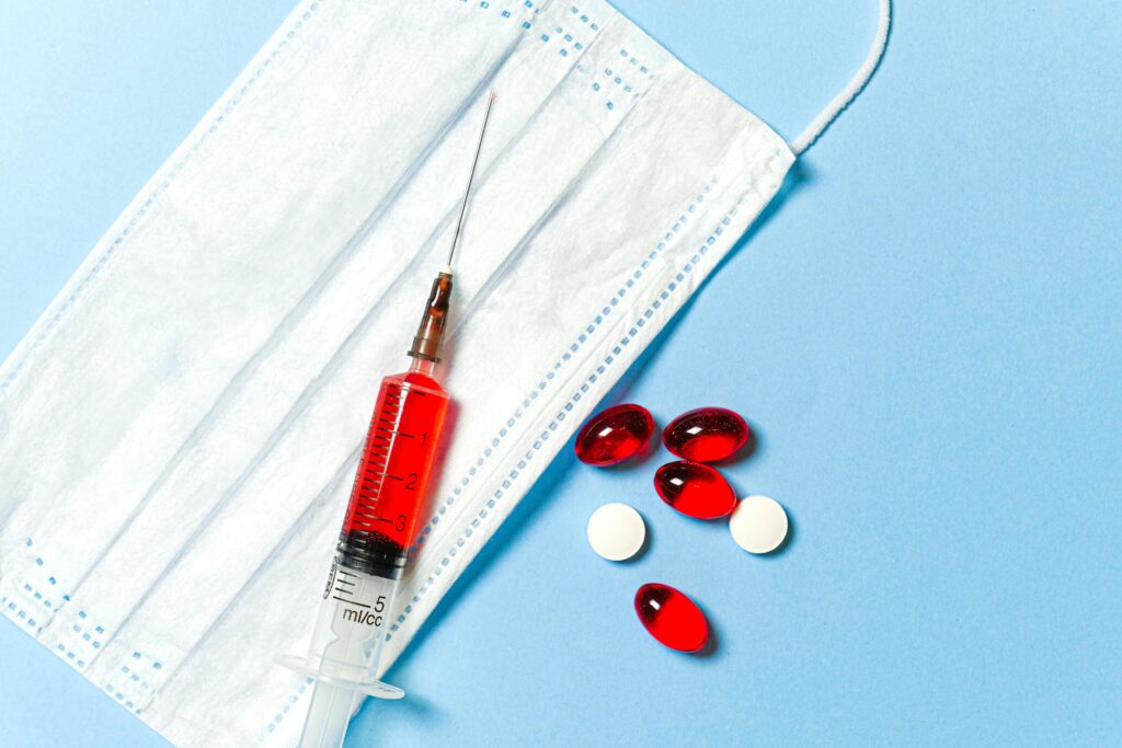 pexels-photo-3786156-3786156 A syringe, face mask, and pills on a blue surface, symbolizing medical treatment.